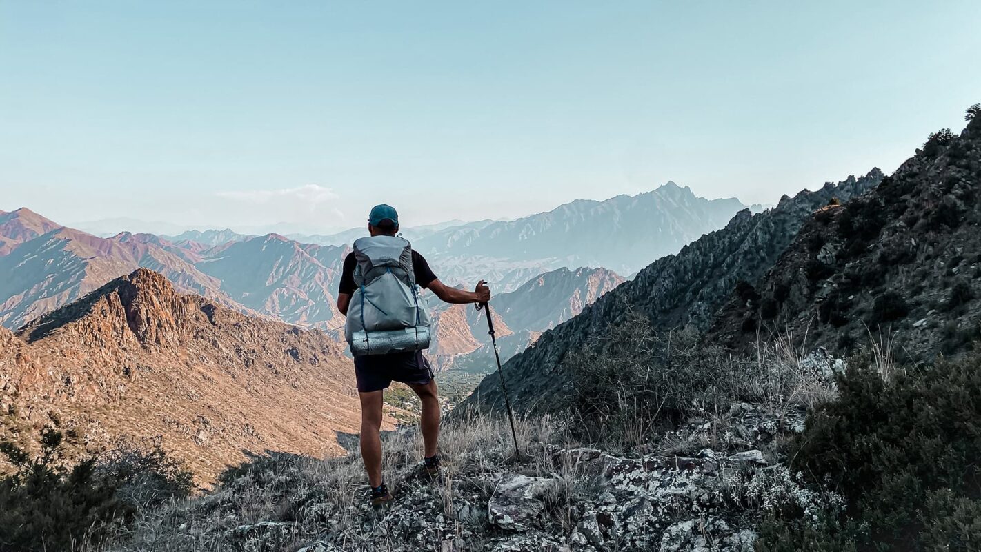Person with big backpack looking out over rugged mountain peaks