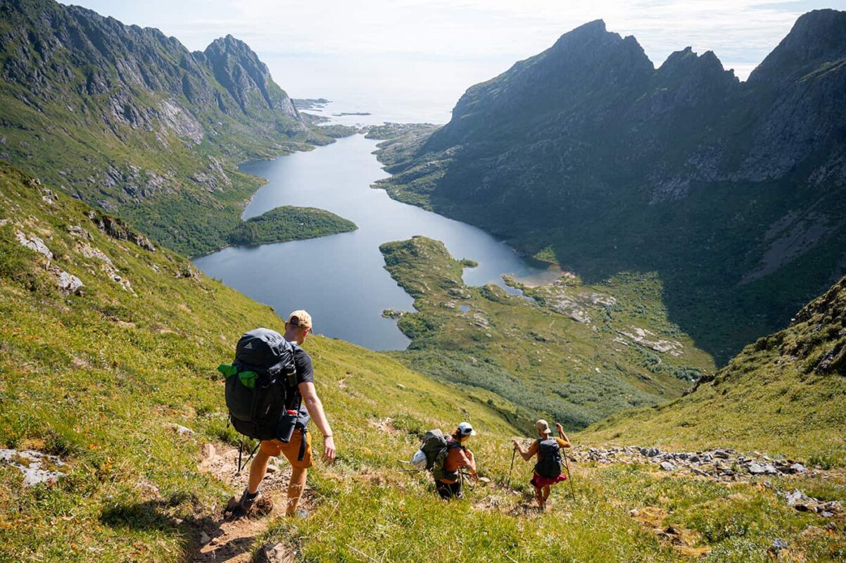 three persons hiking down towards body of water