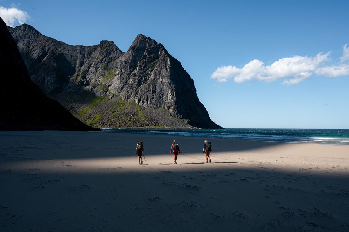 three persons walking on beach with mountains in background