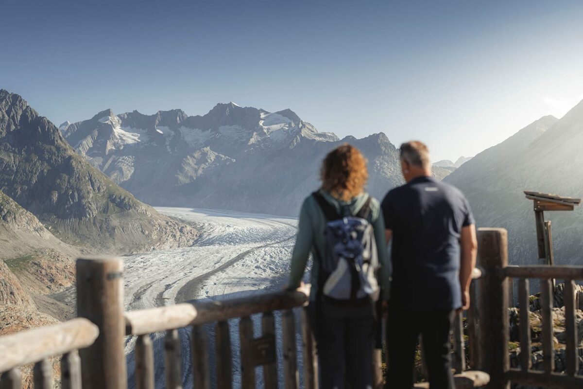 two persons standing at vantage point looking at a glacier