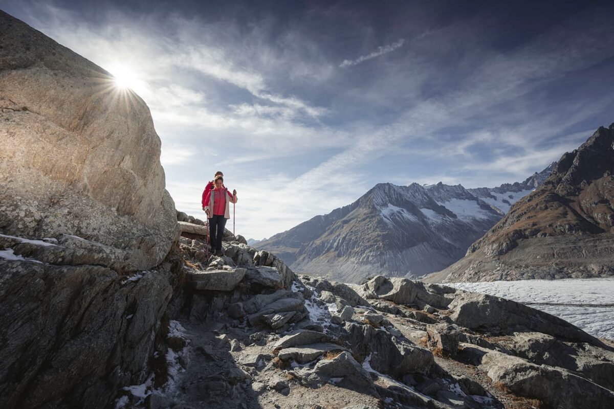 two persons hiking down rocky path near glacier