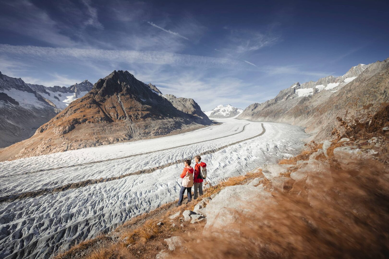 two persons standing on small hiking trail near glacier