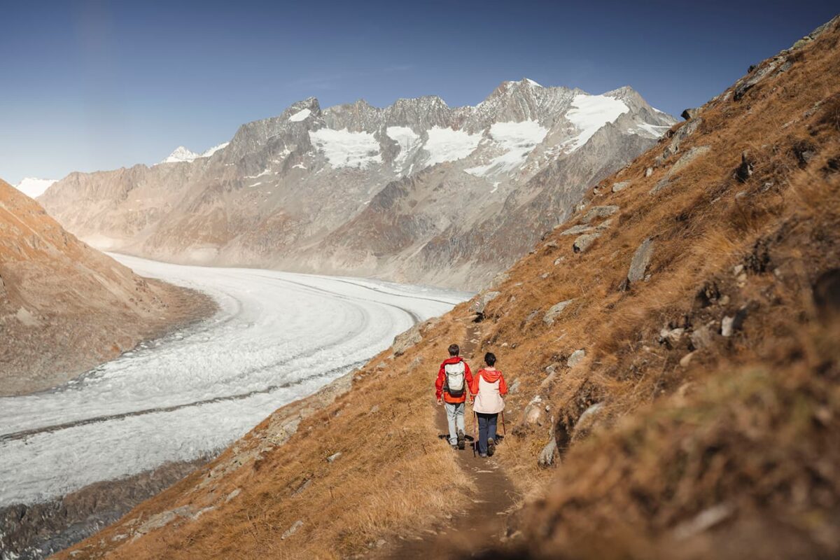 two persons hiking on small hiking trail near glacier