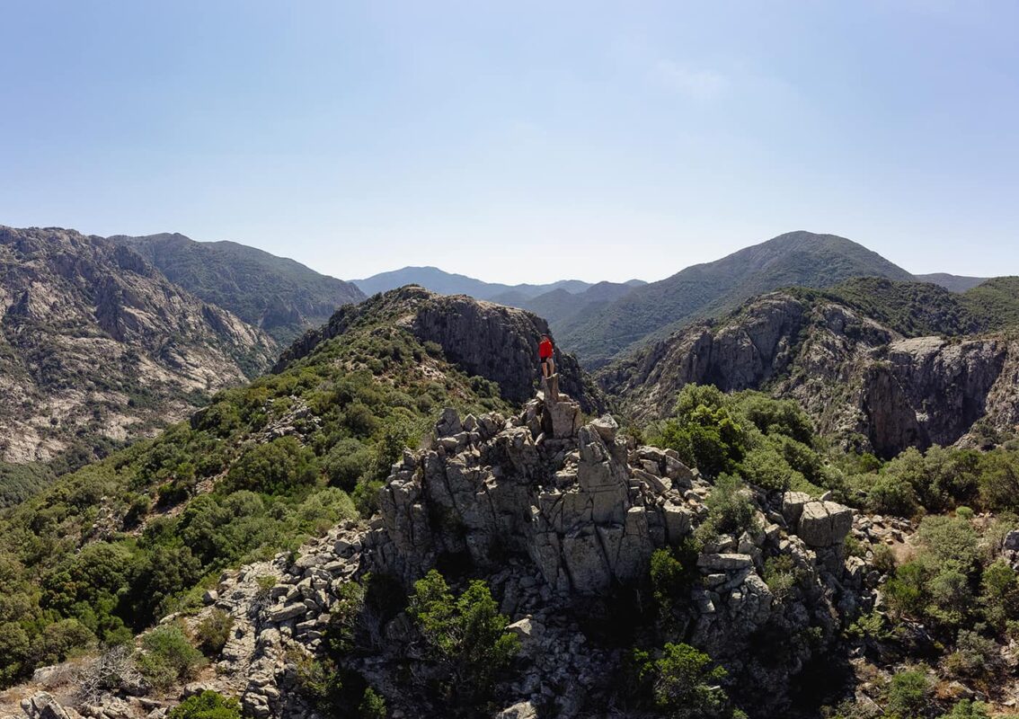 man standing on top of rock formation surrounded by mountains