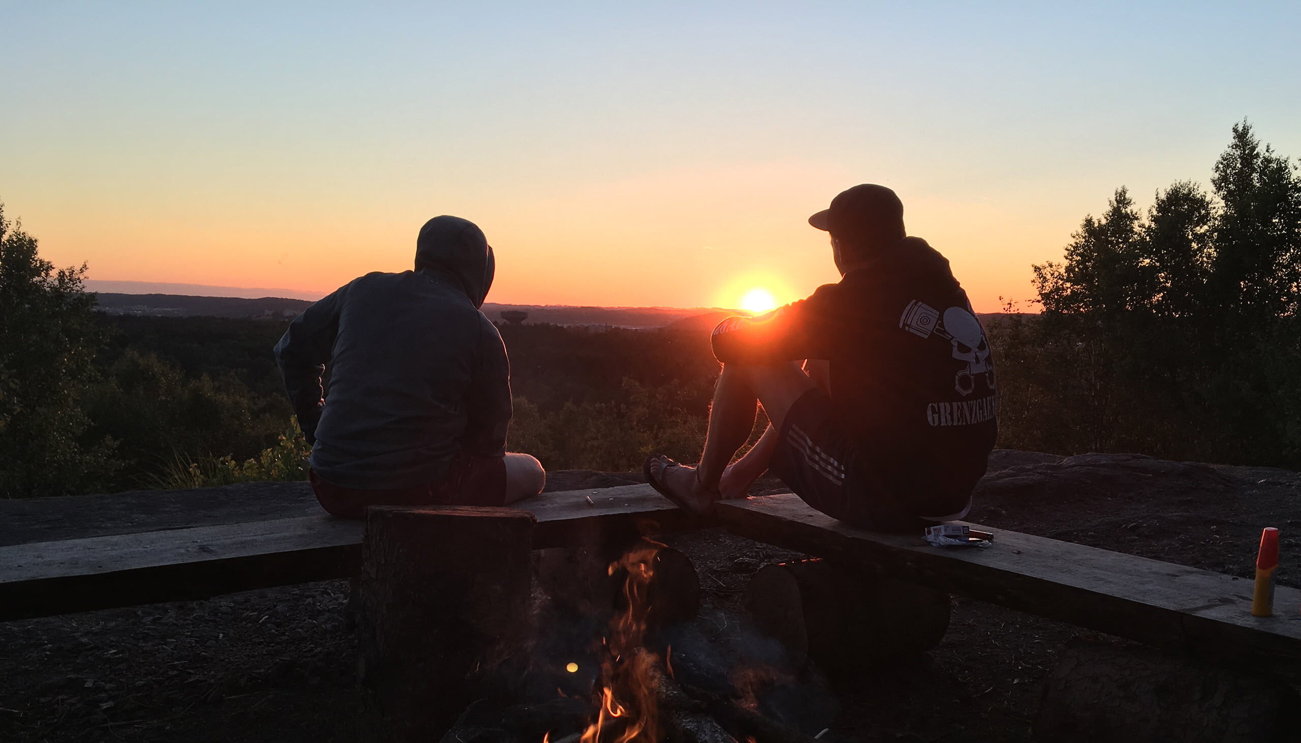 two persons sitting by fire during sunset