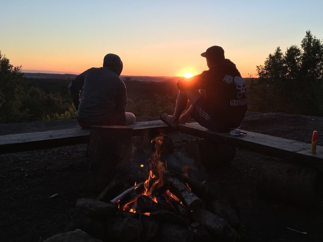 two persons sitting by a fire looking at sunset