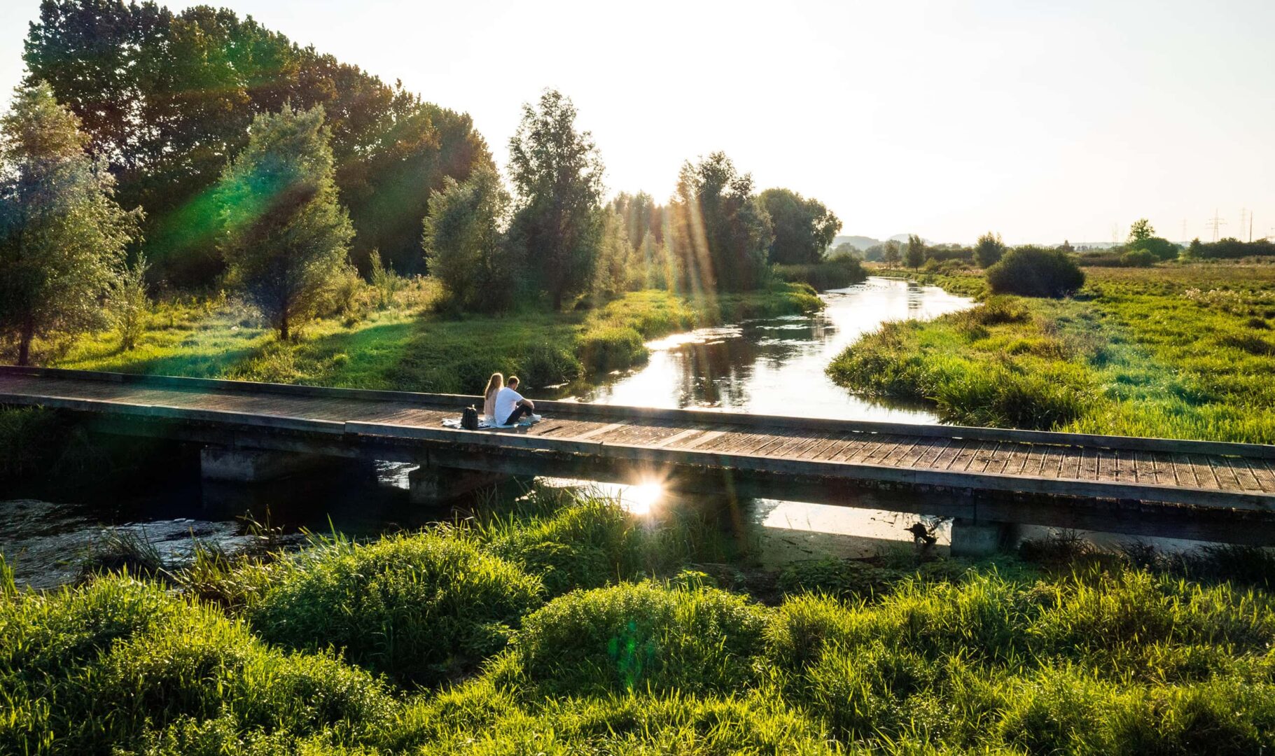 couple sitting on wooden bridge by a river