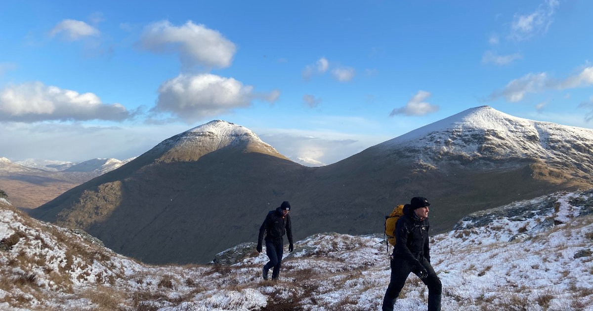 Two men walk through through the scottish peaks with snow on them