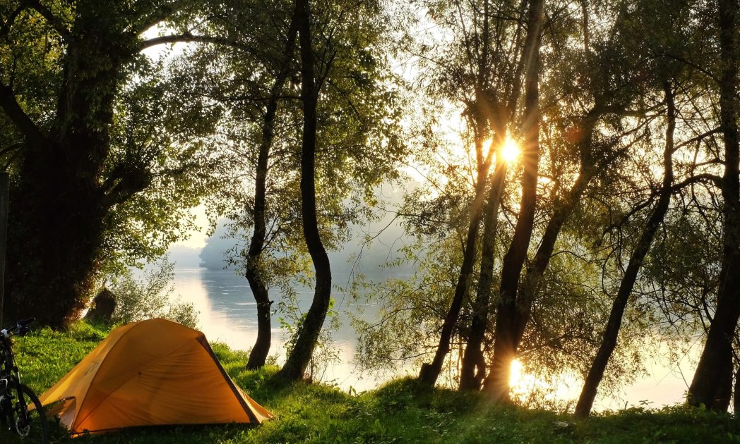 Wild camping in Hungary by a river with soft sunlight through the trees