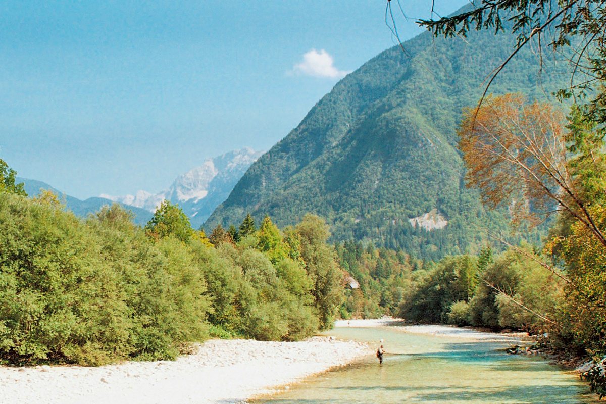 People walking along the banks of the Soca River with mountains in the background