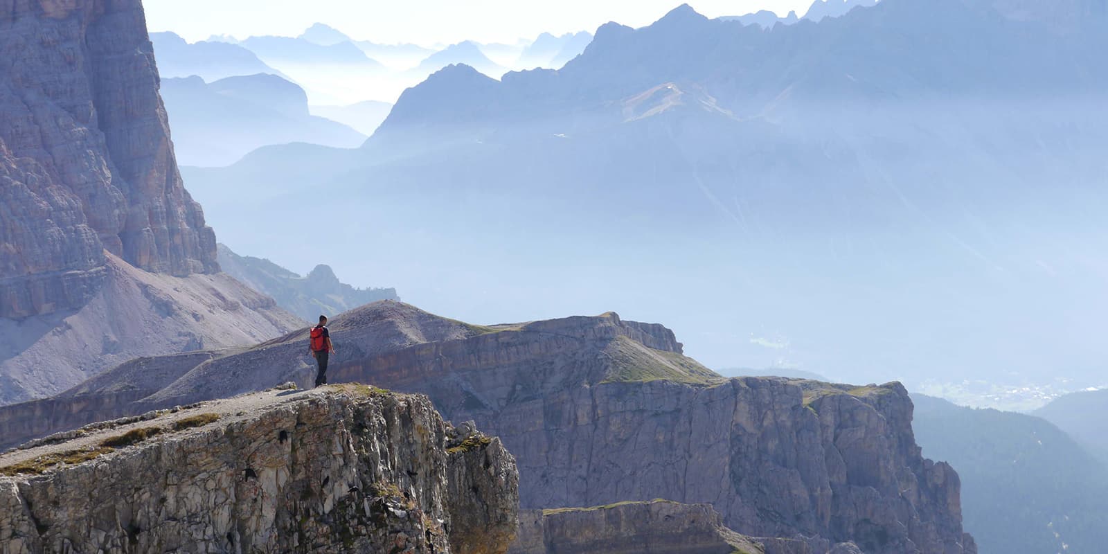 person standing on mountain cliff looking out over Dolomites mountains