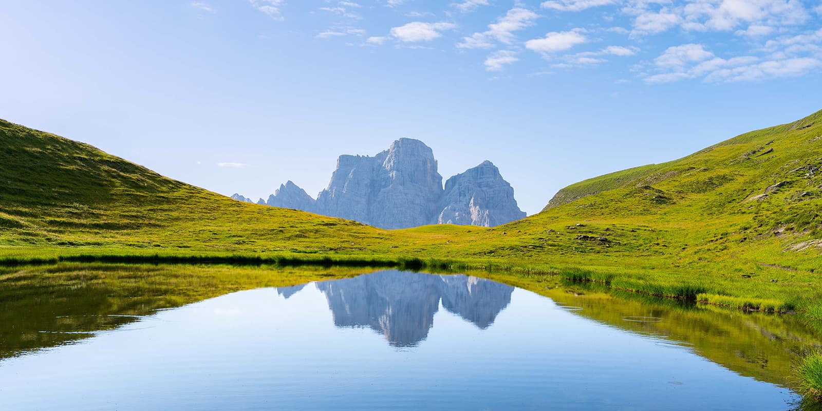 reflection of Dolomites mountains in still water lake surrounded by green hills