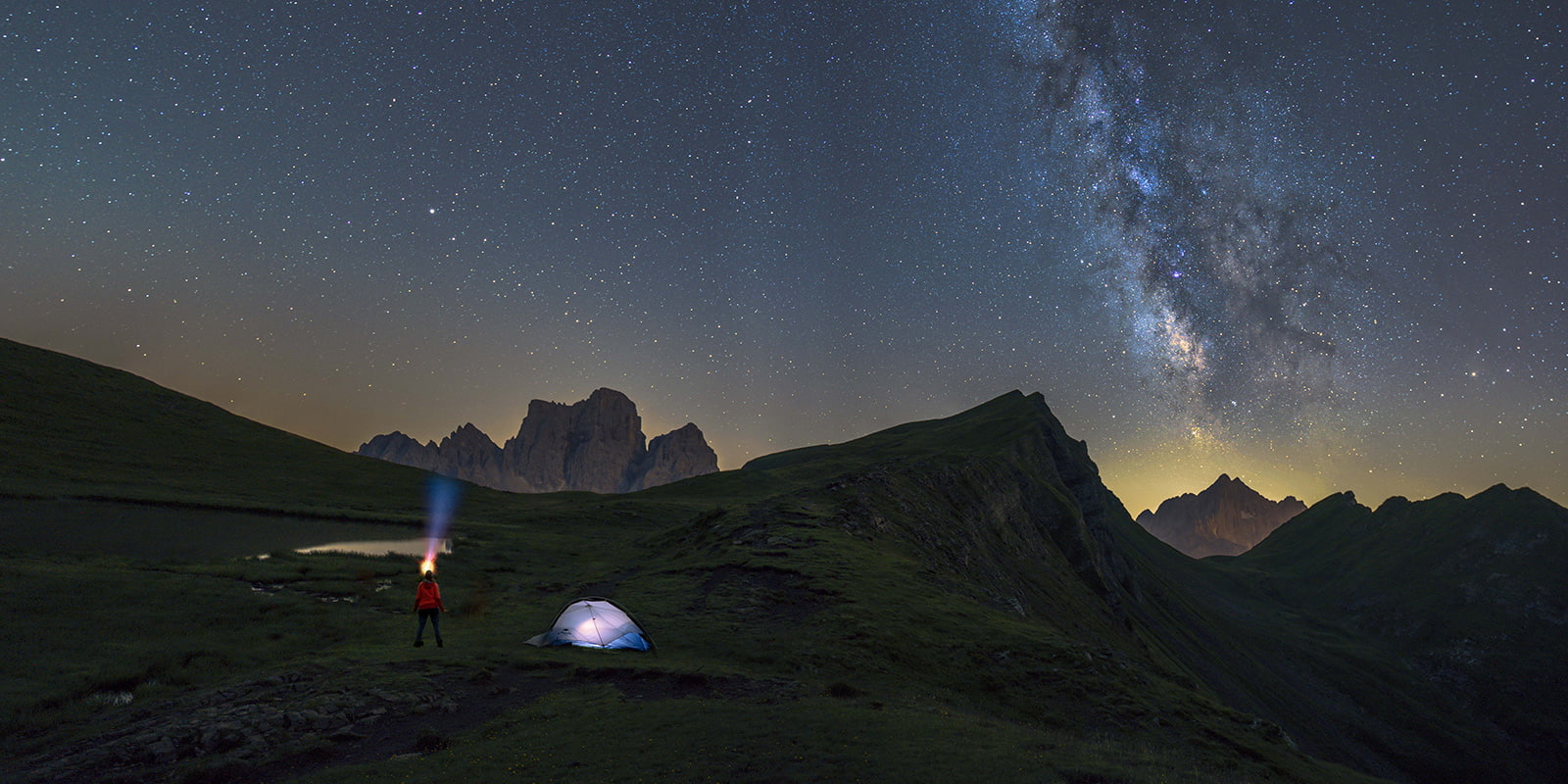 person standing outside by his tent in the night looking into night sky