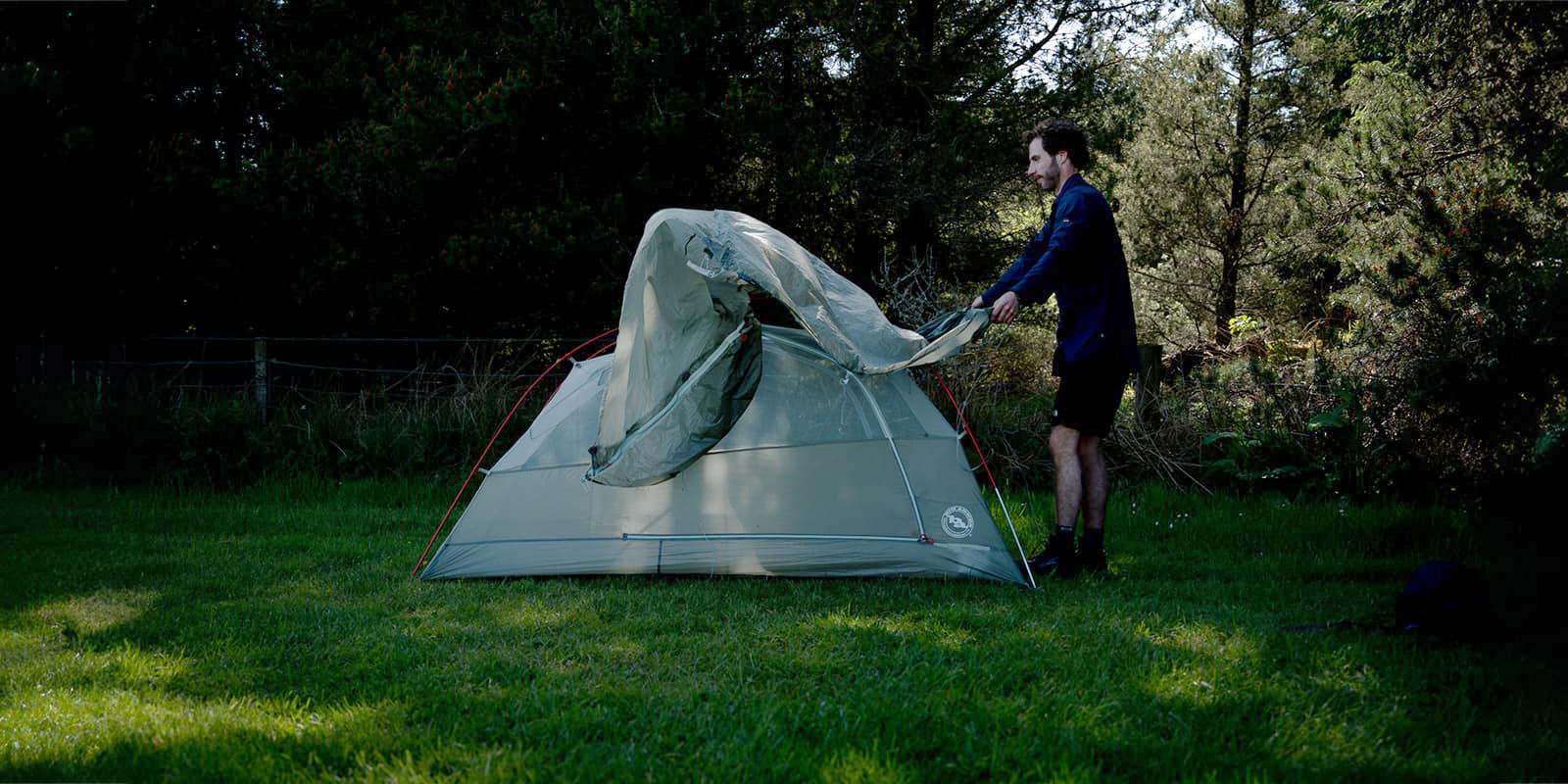 person pitching his tent on grassy field near forest