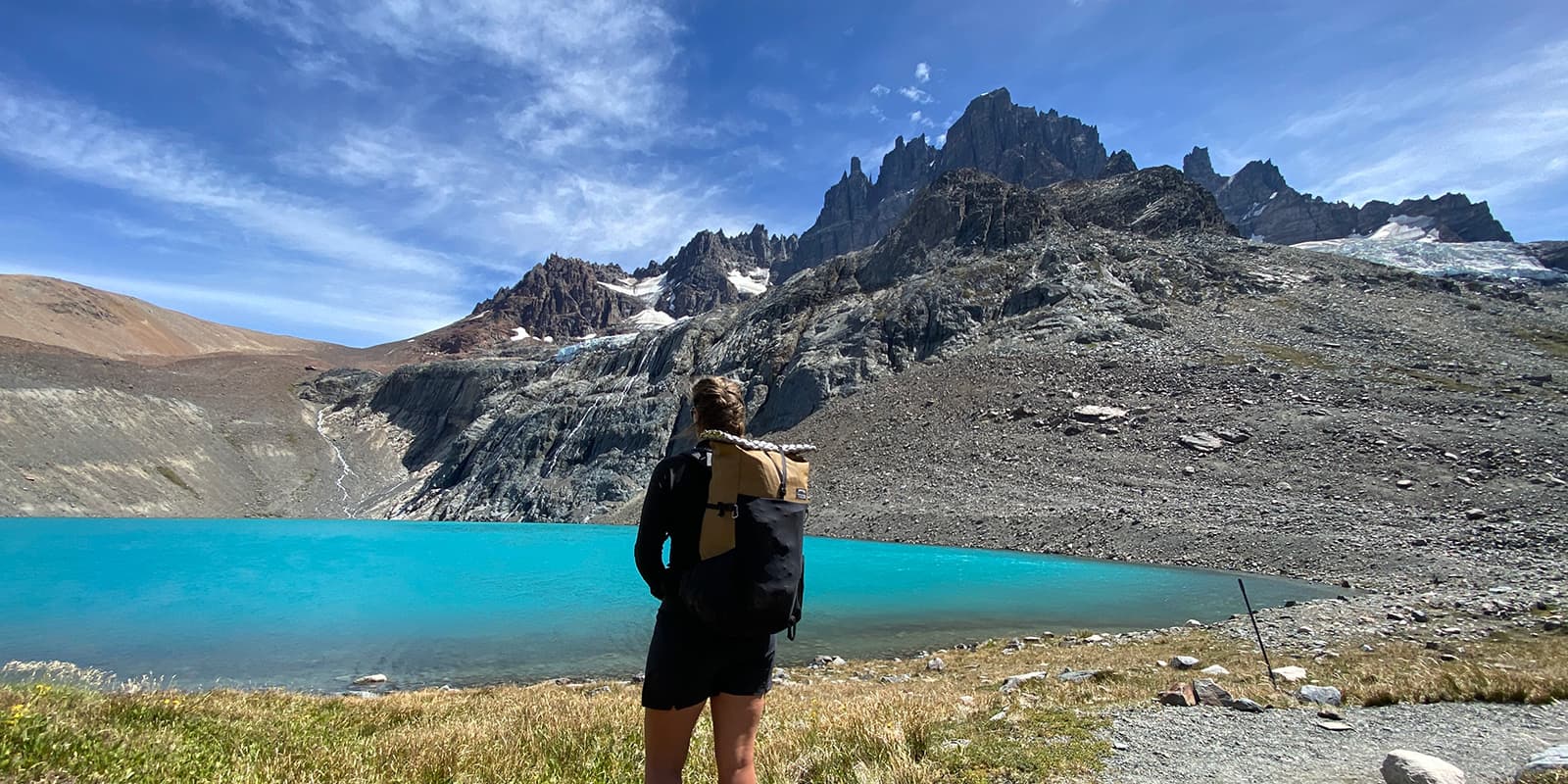 women standing in front of blue lake with rugged peaks in the background