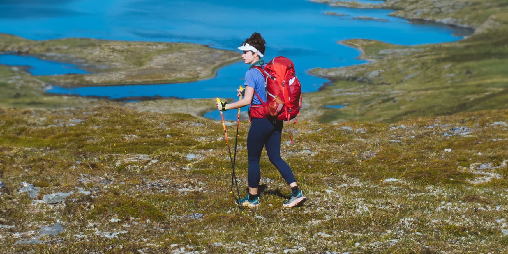 women with red backpack hiking in green field near body of water