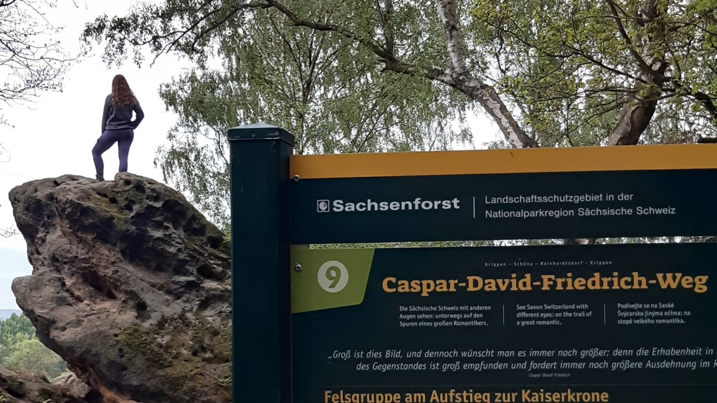 women standing on rock with information sign in the foreground