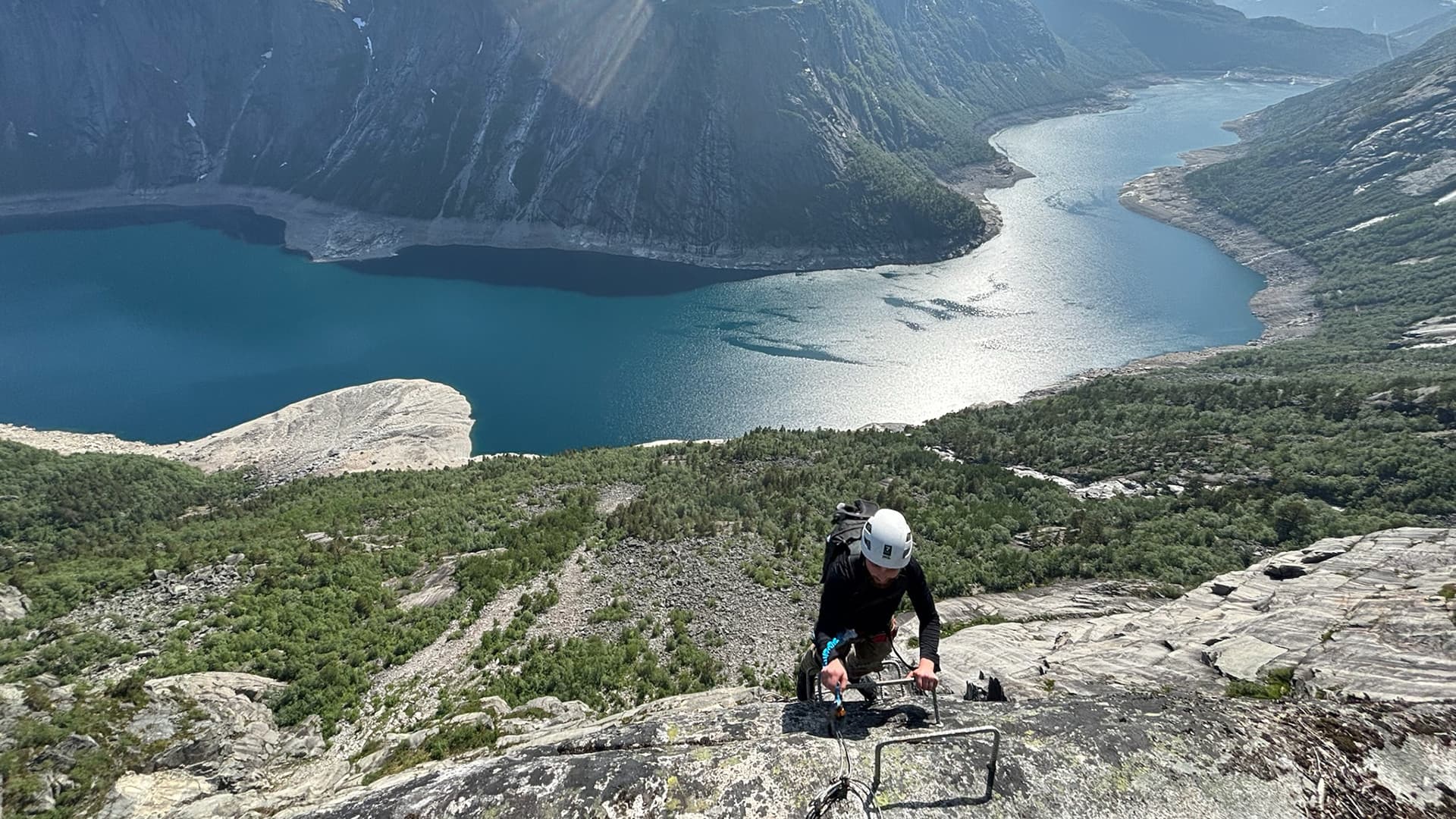 person climbing up steep mountain cliff near Trolltunga valley