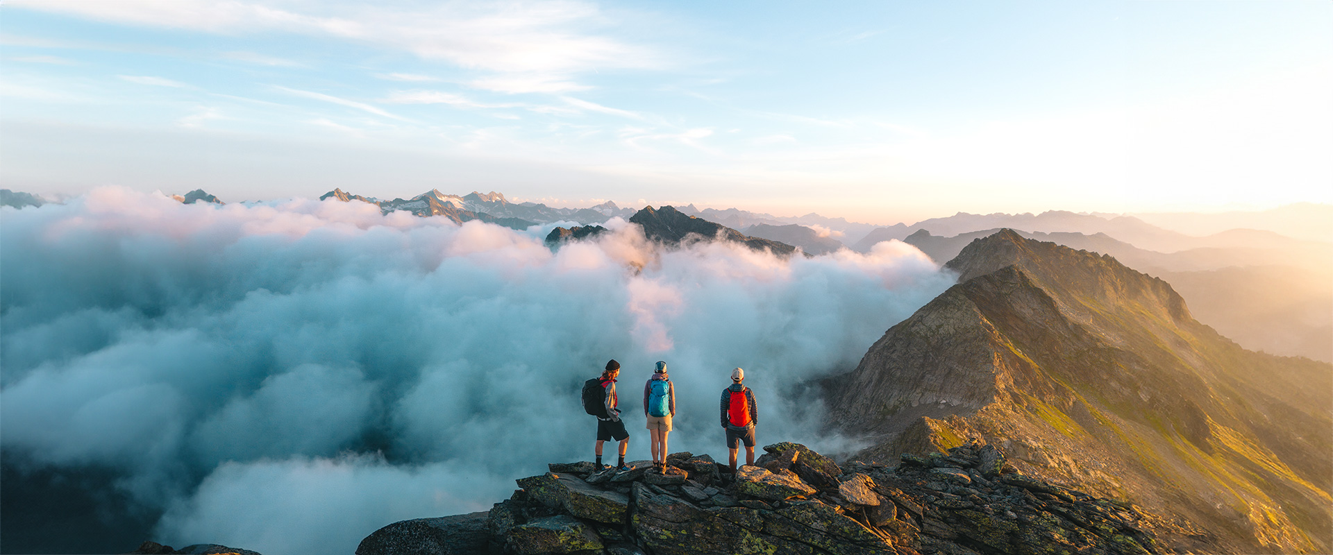 three persons standing on mountain peak with sunrise on the trekking dei Laghetti