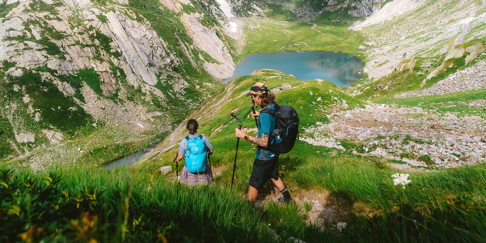 two persons hiking down grassy mountain path