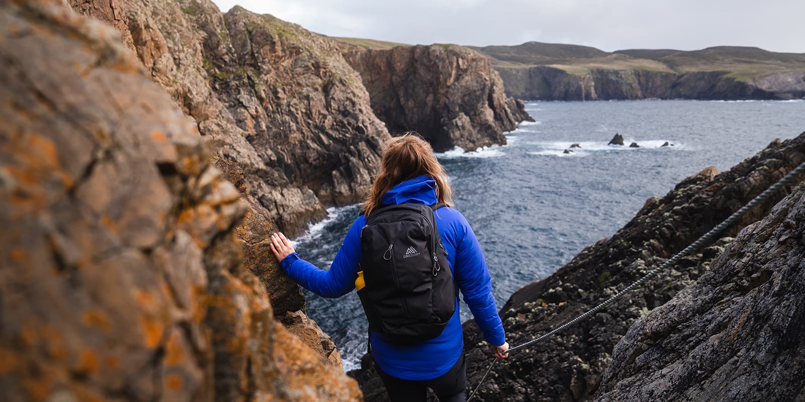 person with Gregory backpack near rugged coastline