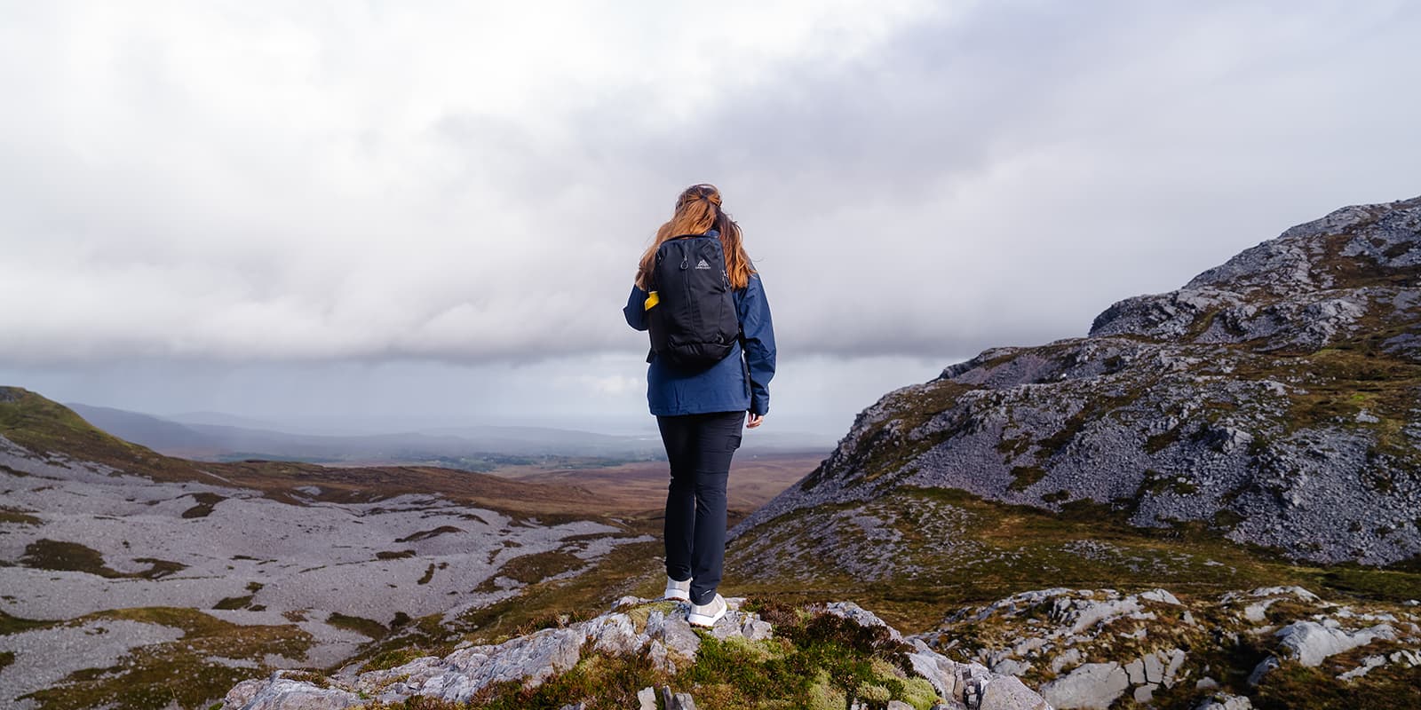 person with Gregory backpack standing on rock overlooking the Irish landscape