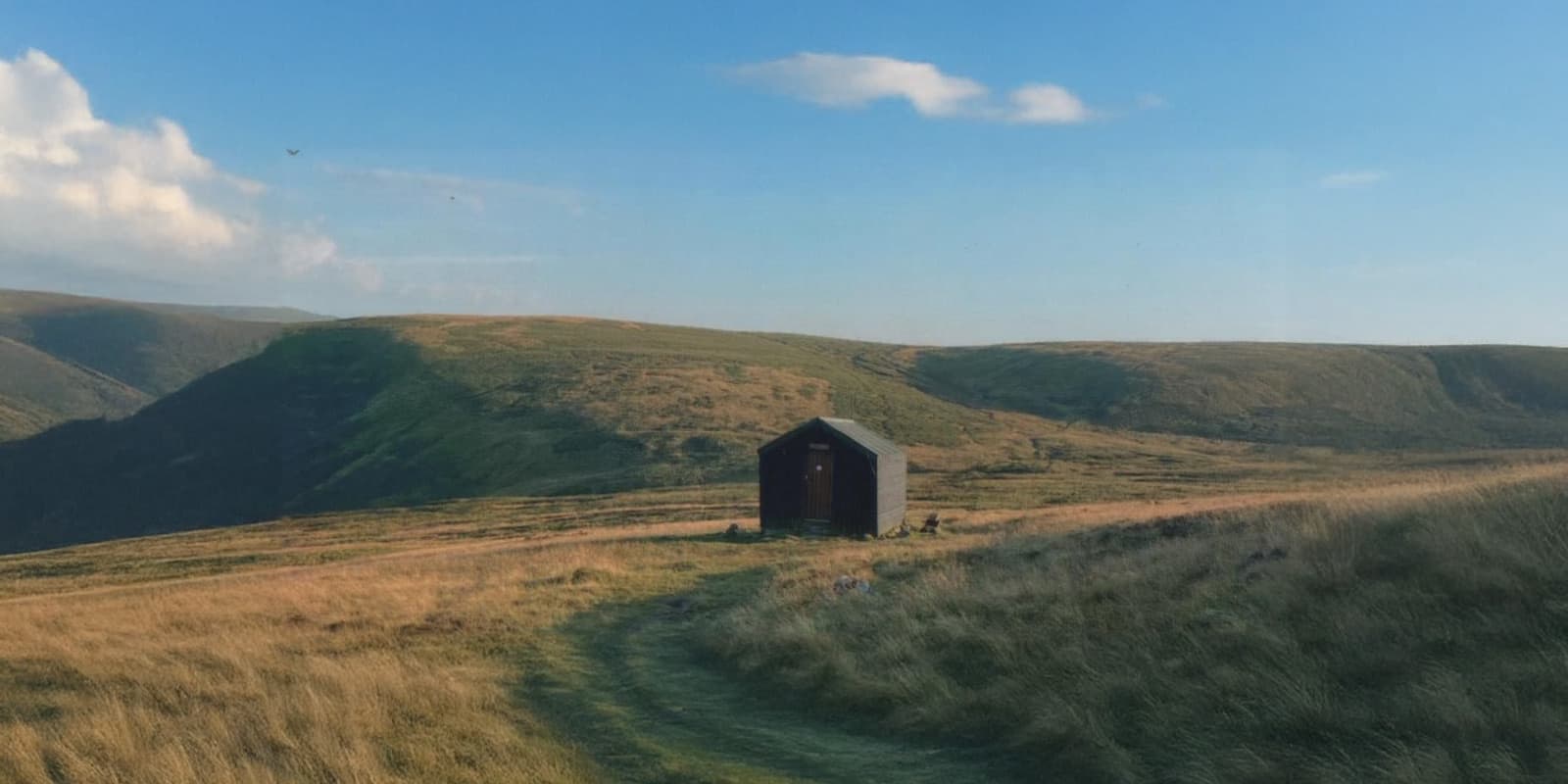 small wooden cabin in grassy field near hills