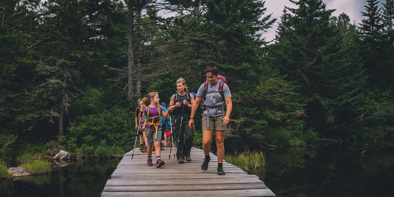 group of young kids hiking over wooden bridge