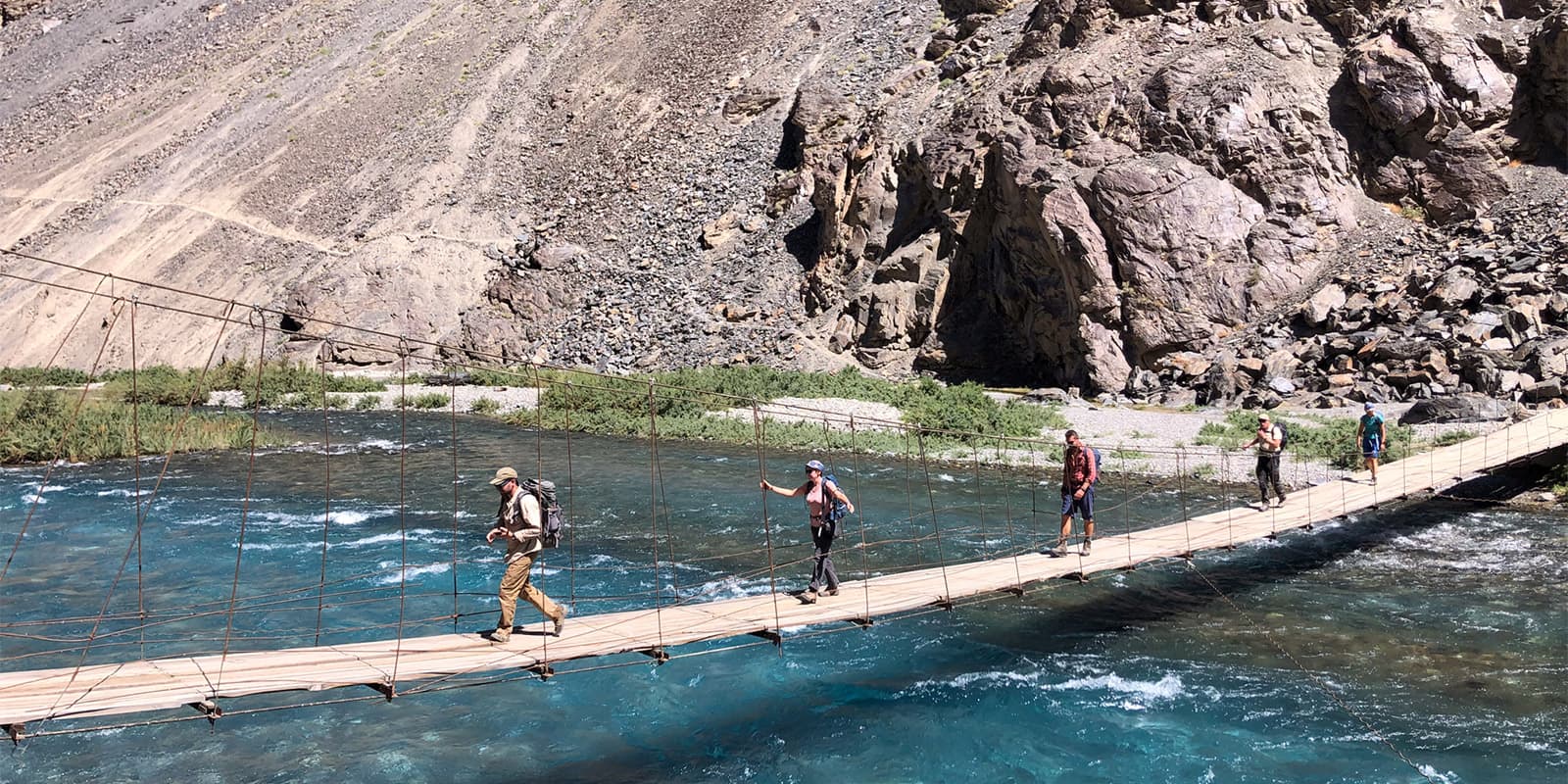 group of people walking across suspension bridge over river in Tajikistan