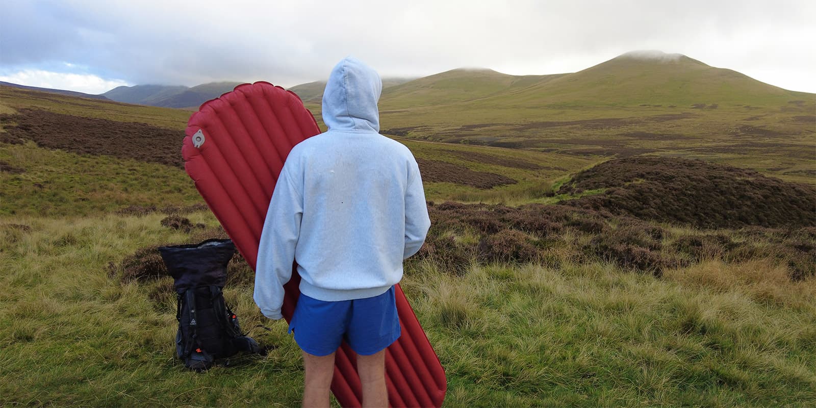 man holding sleeping mat in green hills