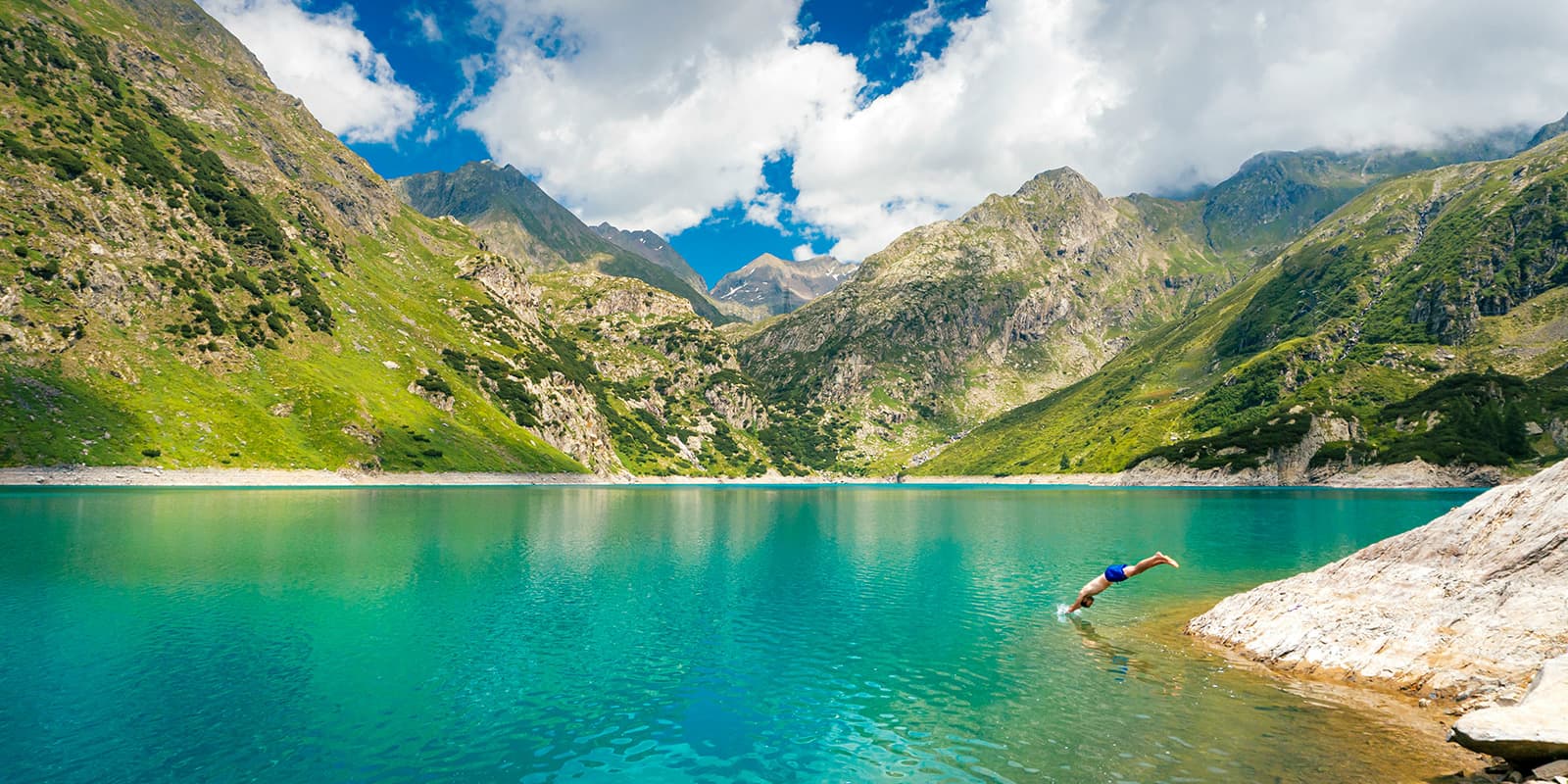 man diving into blue mountain lake in the Italian Alps