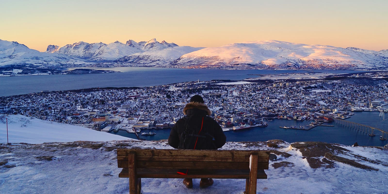 man sitting on bench overlooking the town of Tromso, norway