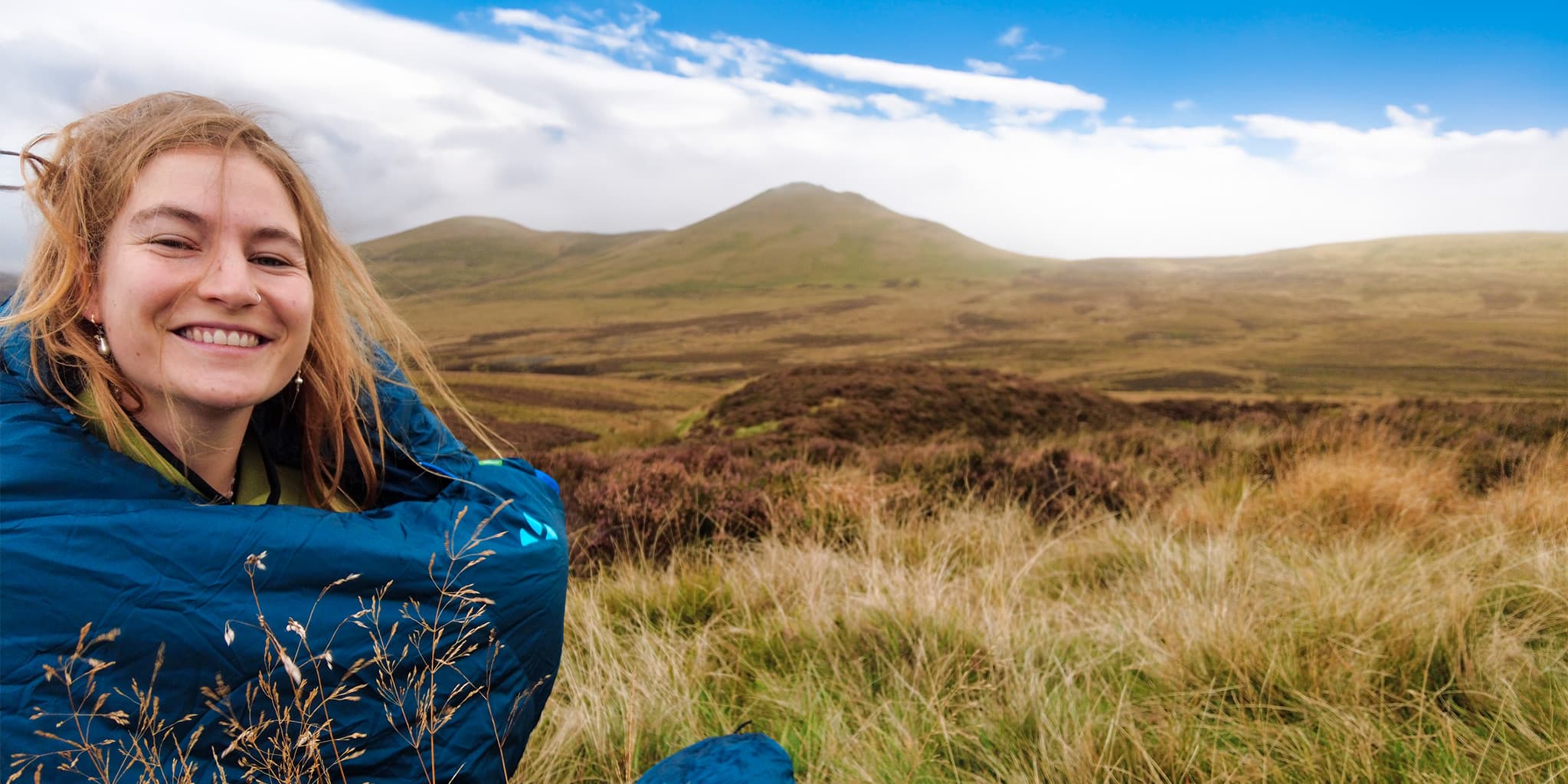 person in sleeping back in the grass with green hills in background