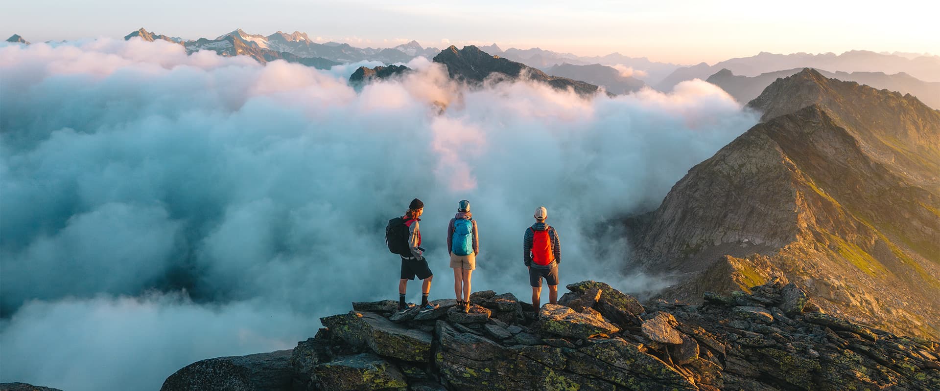 three hikers standing on top of a mountain with sunrise wearing Gregory Kiro backpacks