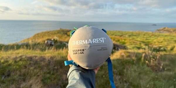 person holding a packed sleeping bag from Thermarest with ocean in the background