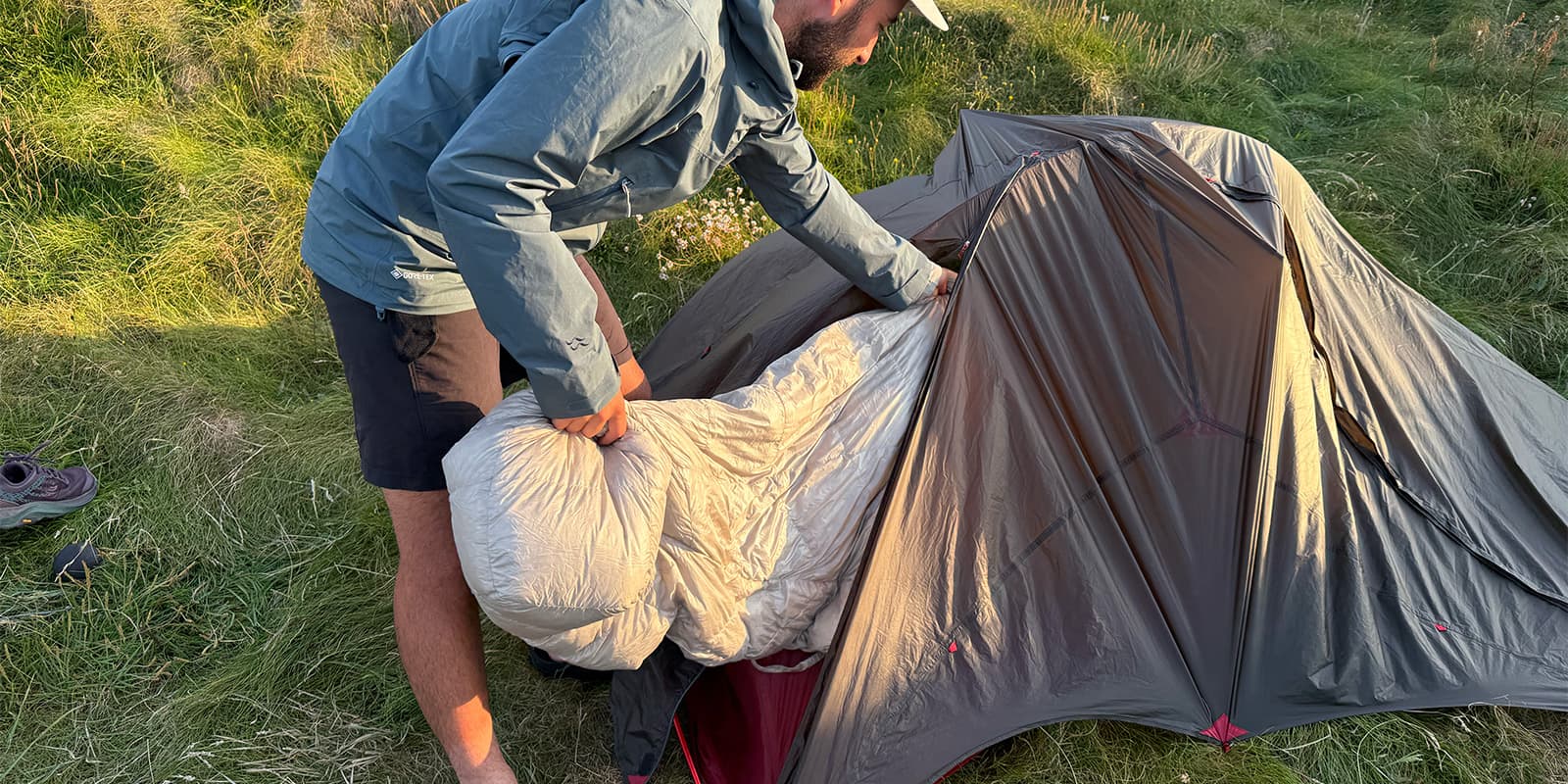 person putting a sleeping bag into a tent on green field