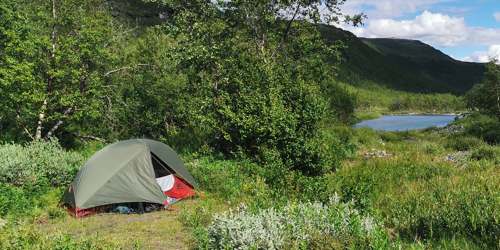 MSR Huba NX solo tent in a clearing near a lake and mountains