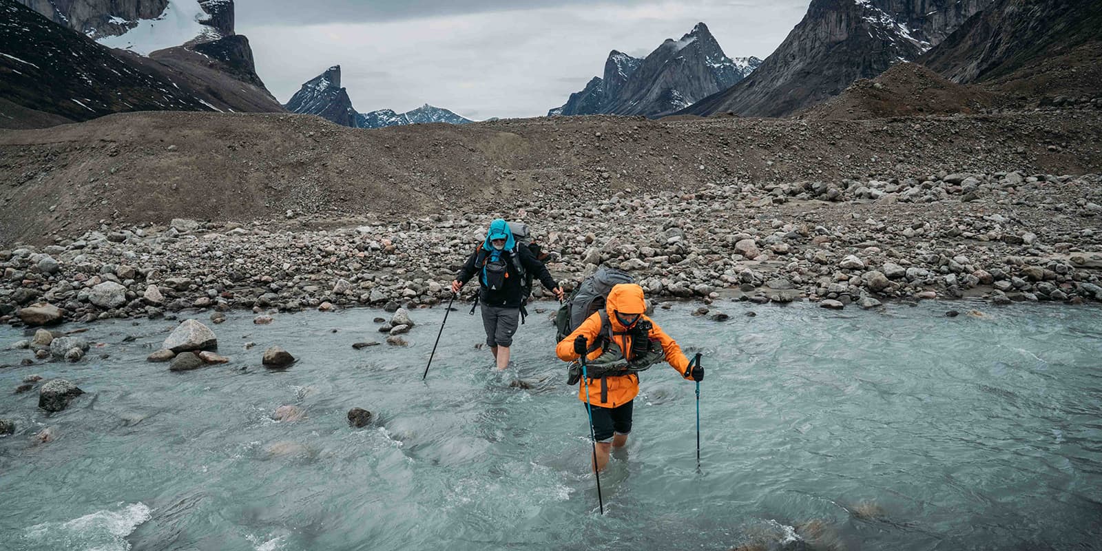 two hikers passing through shallow river on the Akshayuk Pass hiking trail