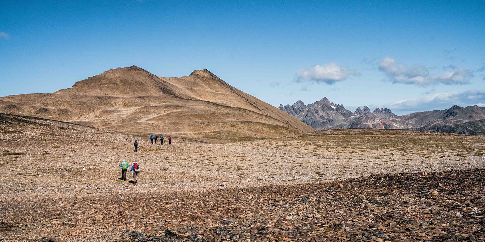 group of hikers hiking towards rugged peaks in the background