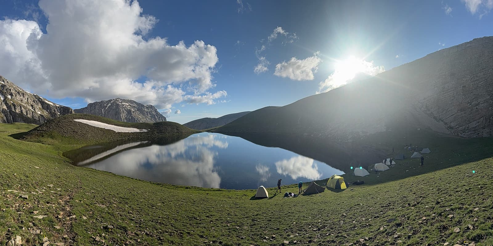 wide angle shot of a mountain lake with hikers pitching tents on the Pindos Horseshoe trail in Greece