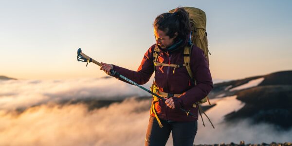 women adjusting her Leki hiking poles on top of a mountain during sunrise