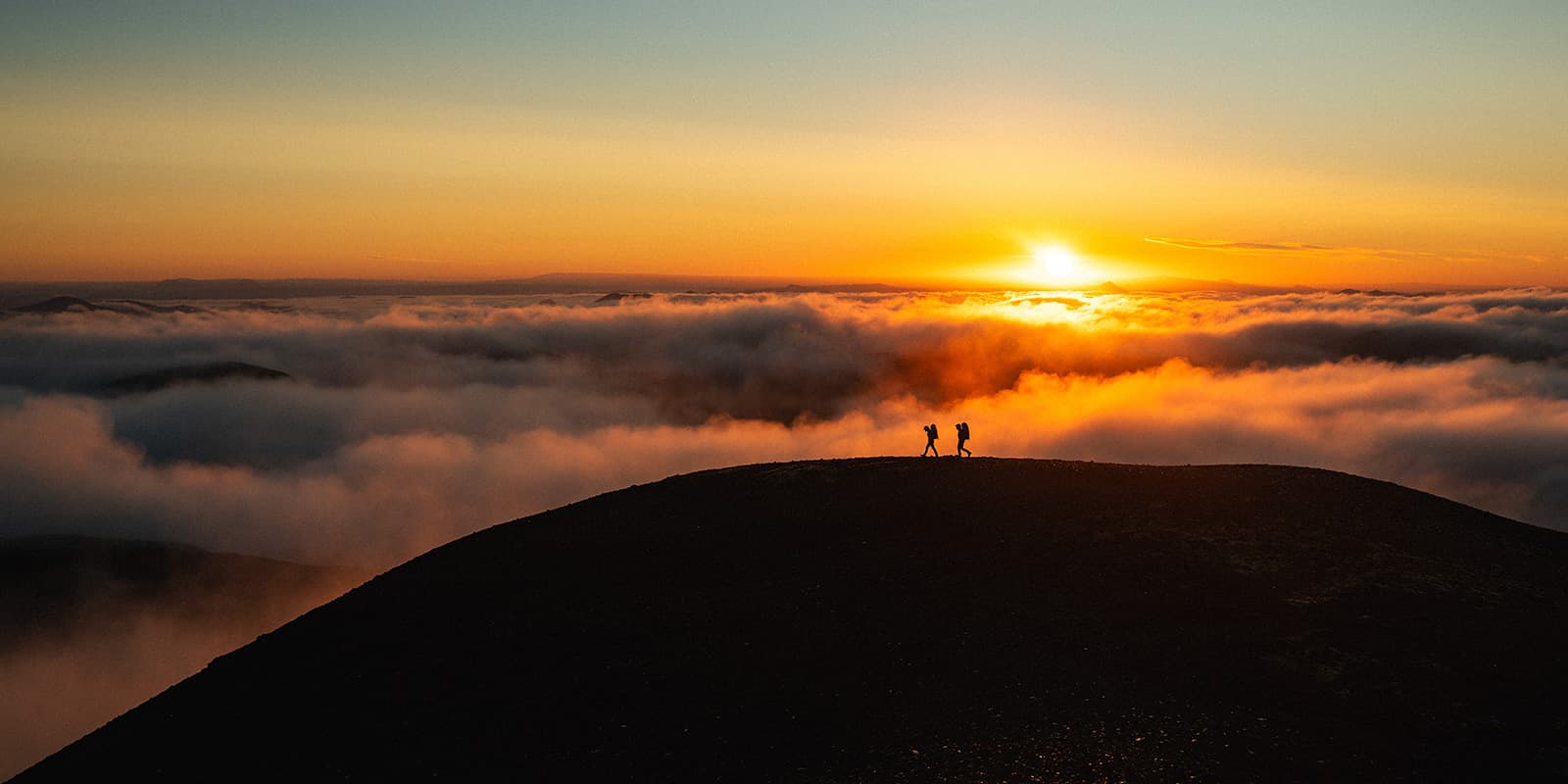 sunrise in Iceland with two hikers in the foreground as silhouettes
