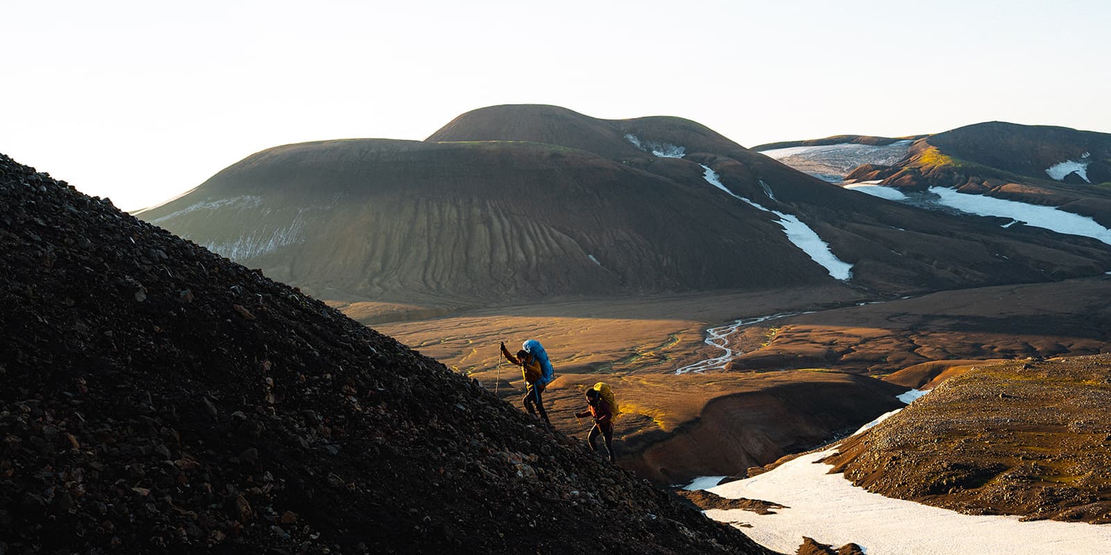 two hikers climbing steep hill in Iceland during sunrise